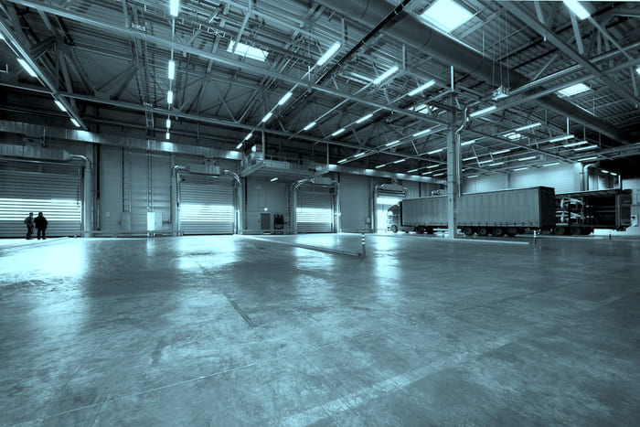 Leere Lagerhalle mit zwei LKWs mit Anhänger – Symbol für die gewerbliche Immobilienversicherung von RIANEVA, die umfassenden Schutz für Geschäftsgebäude bietet.