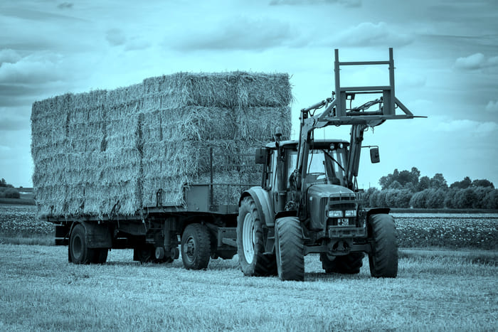 Ein Traktor mit Anhänger und Heugabel – Symbol für die Landwirtschaftliche Fahrzeugversicherung von RIANEVA, die Schäden an landwirtschaftlichen Maschinen und Fahrzeugen absichert.