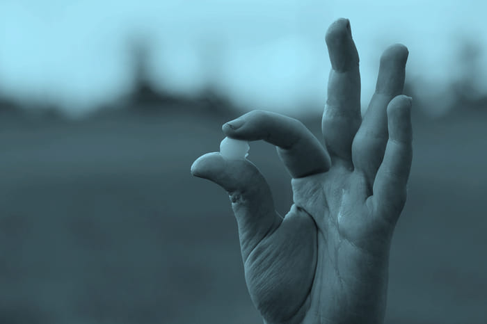 Eine Hand, die eine Hagelkugel zwischen Daumen und Zeigefinger hält – repräsentiert die Hagelversicherung von RIANEVA, die Schutz vor Schäden durch Hagel bietet.