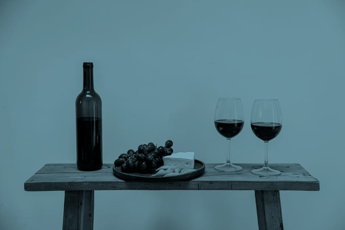 Buschenschanktisch mit Weinflasche, Weingläsern und Heurigen Brettjause – Symbol für die maßgeschneiderten Spezialversicherungen von RIANEVA, die Landwirte vor Ernteausfällen und anderen Risiken schützen.