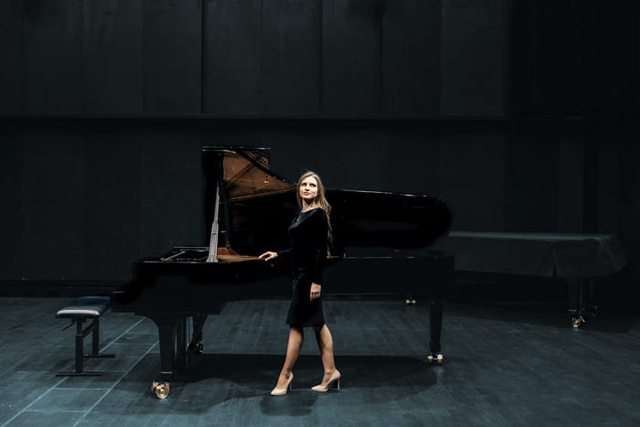 Elegant gekleidete Frau steht vor einem Konzertflügel auf einer Bühne – Symbol für die Spezialversicherungen von RIANEVA, die wertvolle Besitztümer schützen.